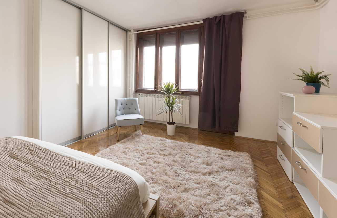 Spavaća soba sa bračnim krevetom, belim ugradnim plakarom i svetloplavom foteljom – Apartman Milica – City Break Apartments