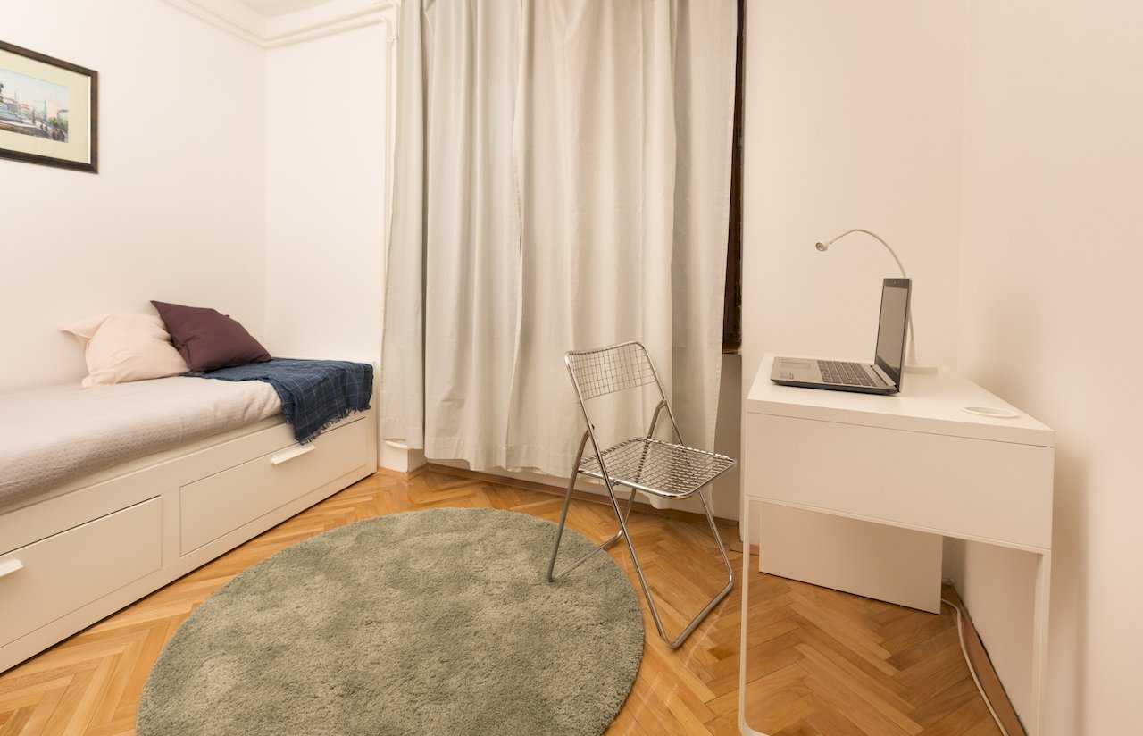 Manja soba sa singl krevetom na fiokama, belim radnim stolom i laptopom – Apartman Milica – City Break Apartments