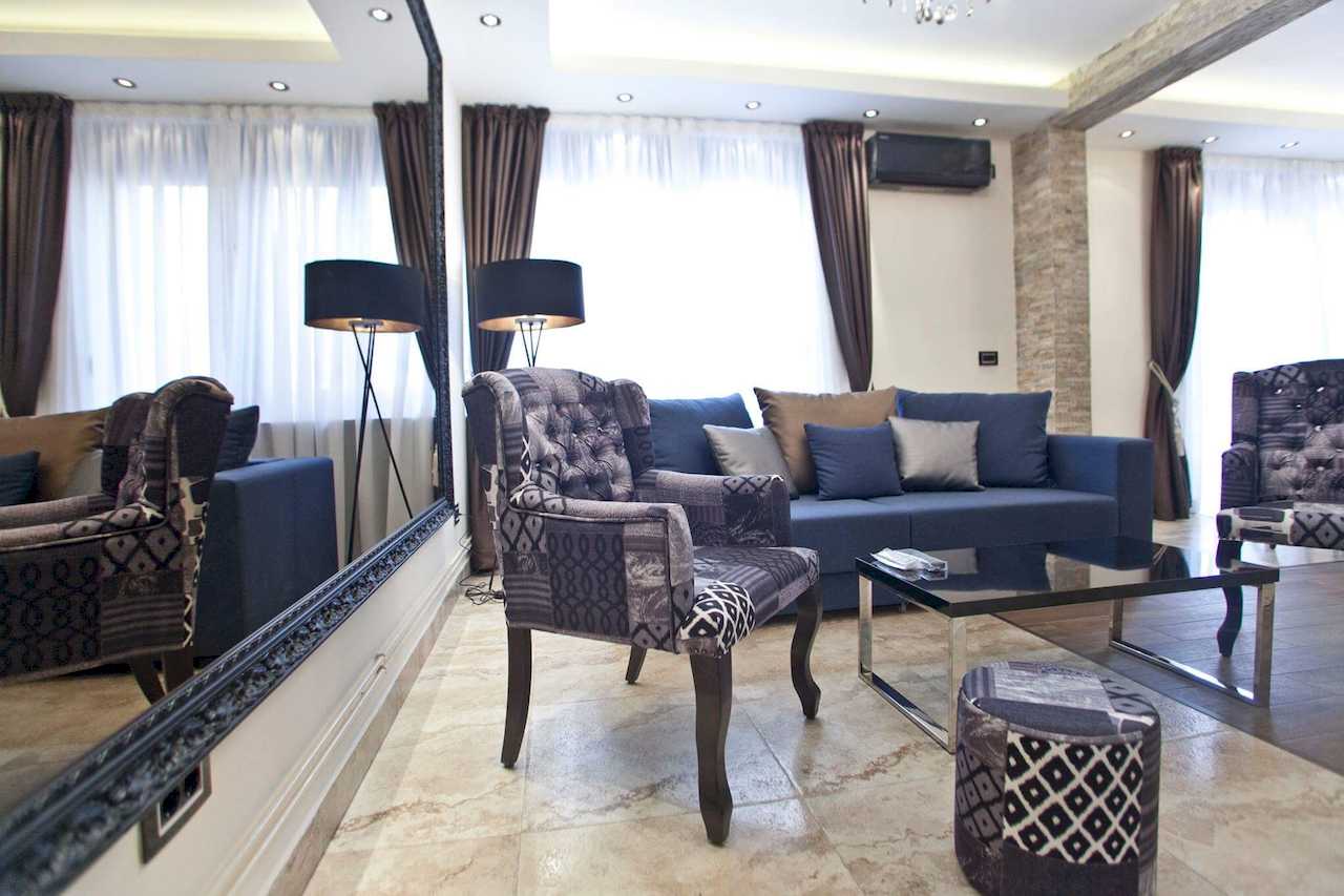 Dnevni kutak sa plavom sofom, patchwork foteljama i velikim ogledalom naslonjenim na zid – Apartman Molerova – City Break Apartments