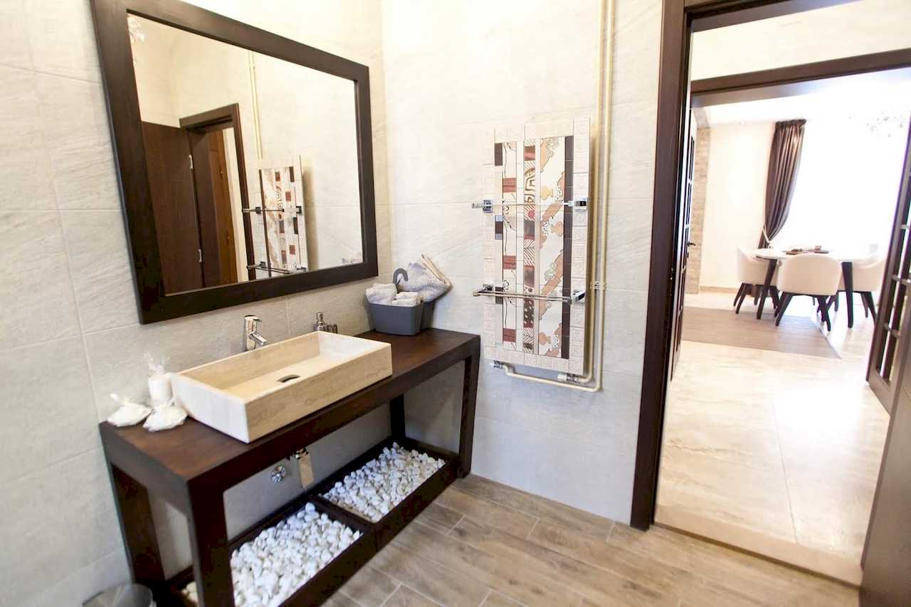 Kupatilo sa kamenim umivaonikom na drvenoj konzoli i pogledom na okrugli trpezarijski sto – Apartman Molerova – City Break Apartments