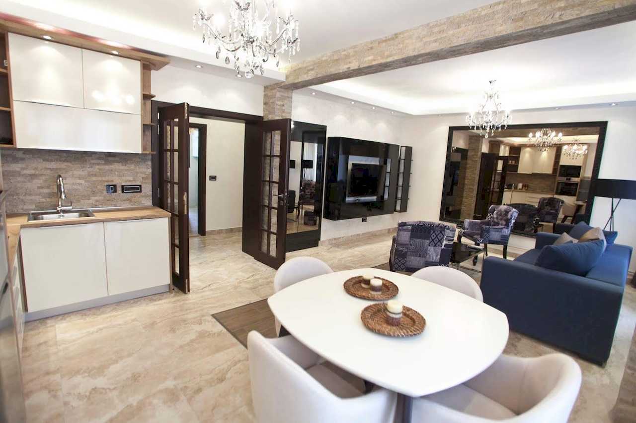 Trpezarija sa belim stolom i četiri stolice, kuhinja i dnevni boravak u pozadini – Apartman Molerova – City Break Apartments