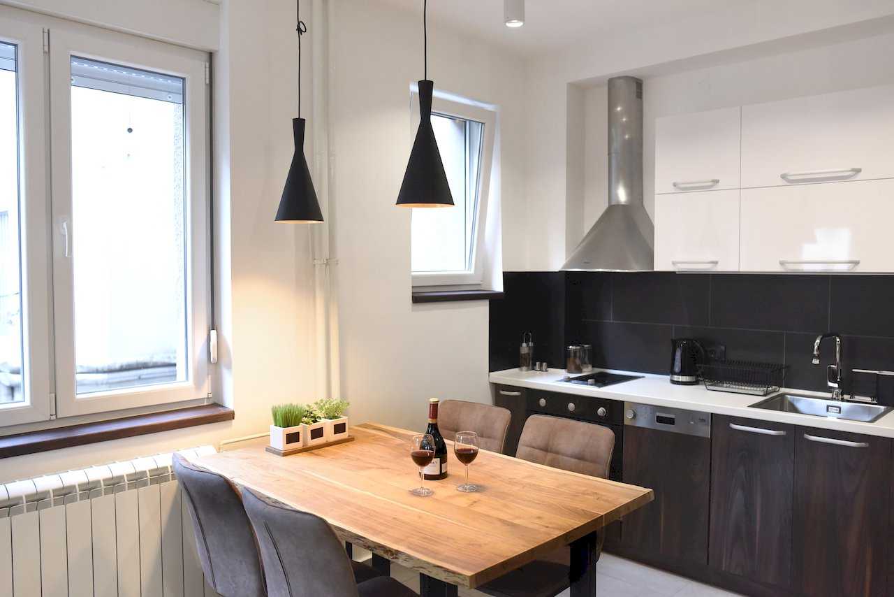 Drveni trpezarijski sto sa sivim stolicama i kuhinja sa crnim pločicama – Apartman Mondo 2 – City Break Apartments