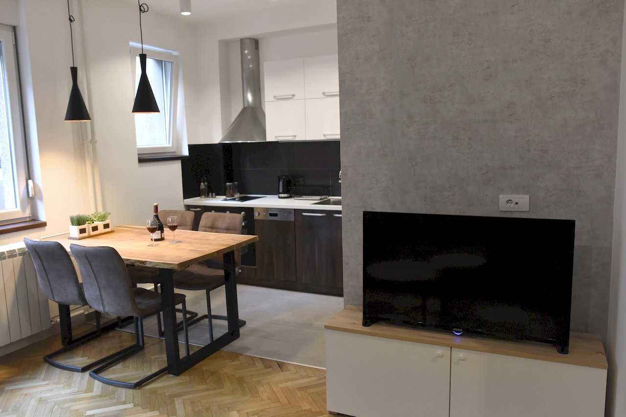 Pogled na TV zonu sa sivim akcent zidom, trpezariju i kuhinju – Apartman Mondo 2 – City Break Apartments