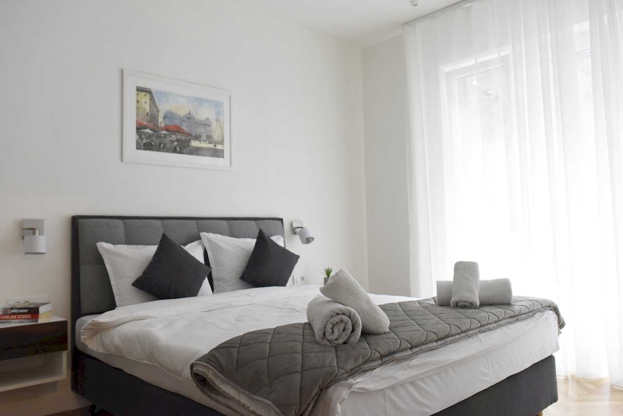 Spavaća soba sa bračnim krevetom, belom posteljinom i uokvirenom slikom iznad uzglavlja – Apartman Mondo 2 – City Break Apartments