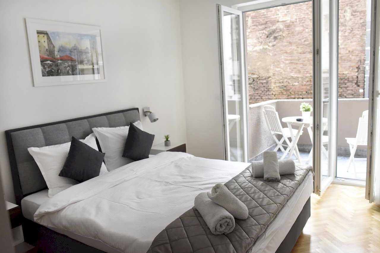 Spavaća soba sa bračnim krevetom i otvorenim izlazom na terasu sa belom garniturom – Apartman Mondo 2 – City Break Apartments
