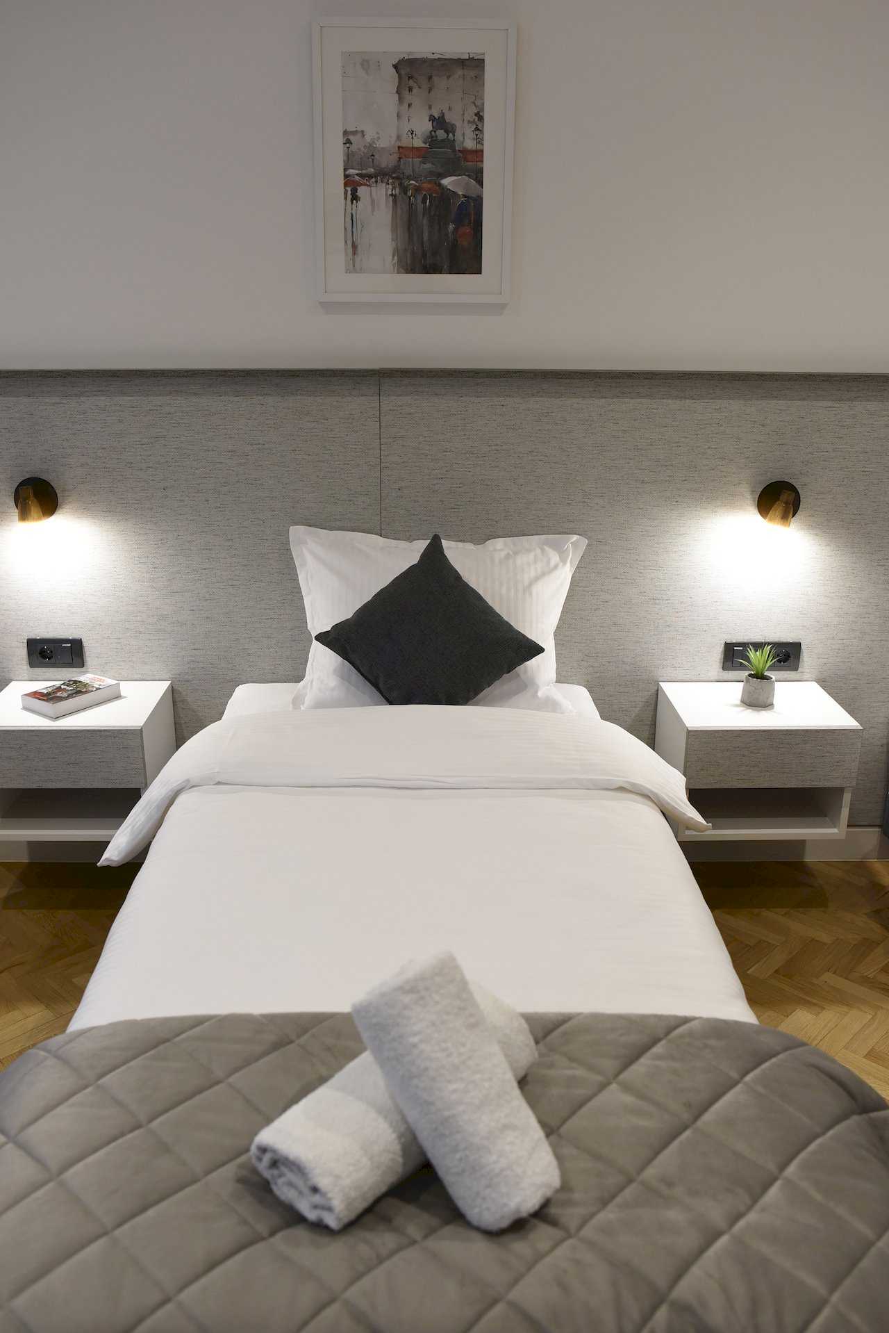 Spavaća soba sa jednim krevetom, širokim sivim uzglavljem i belim noćnim ormarićima – Apartman Mondo 2 – City Break Apartments