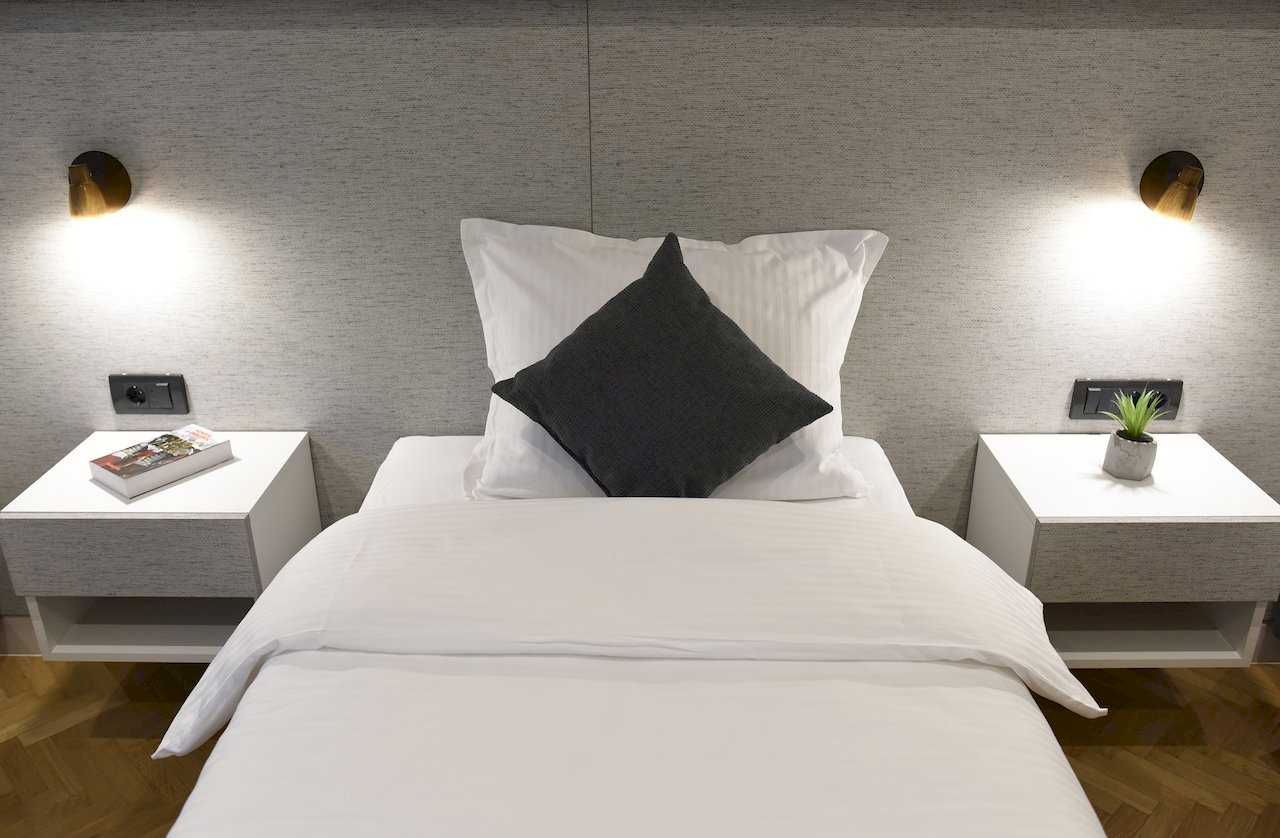 Krupni plan kreveta sa belim noćnim ormarićima i mesingastim zidnim lampama – Apartman Mondo 2 – City Break Apartments