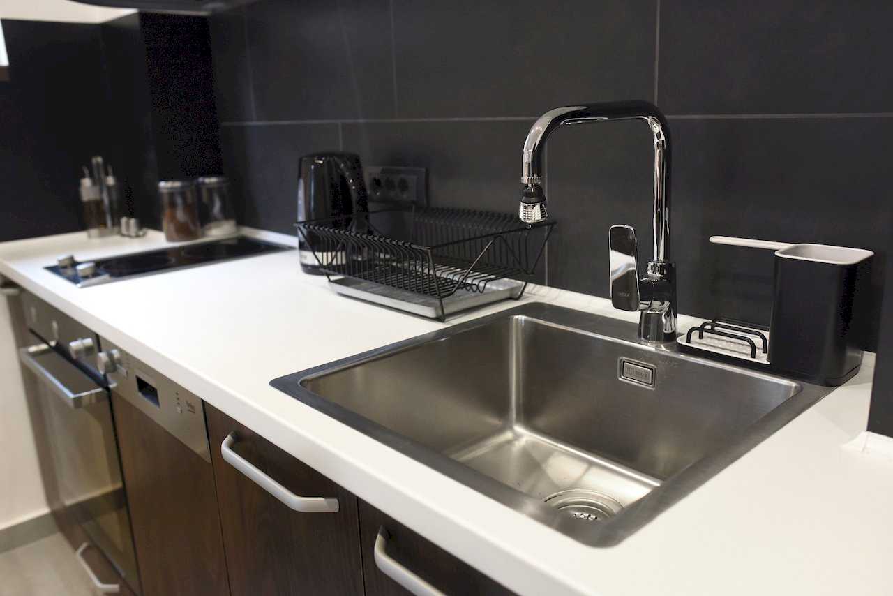 Detalj kuhinje sa sudoperom, ugradnom staklokeramičkom pločom i tamnim elementima – Apartman Mondo 2 – City Break Apartments