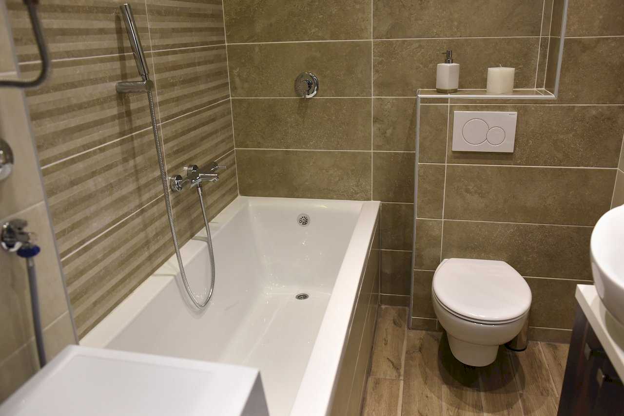 Kupatilo sa ugradnom kadom, konzolnim WC-om i bež pločicama, deo umivaonika – Apartman Mondo 2 – City Break Apartments