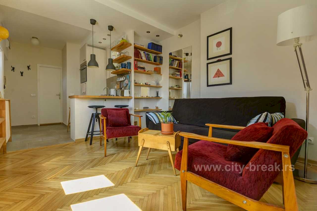 Apartman NINA (Vračar, Beograd) – dnevna sa bordo foteljama, crnom sofom i kuhinjskim šankom