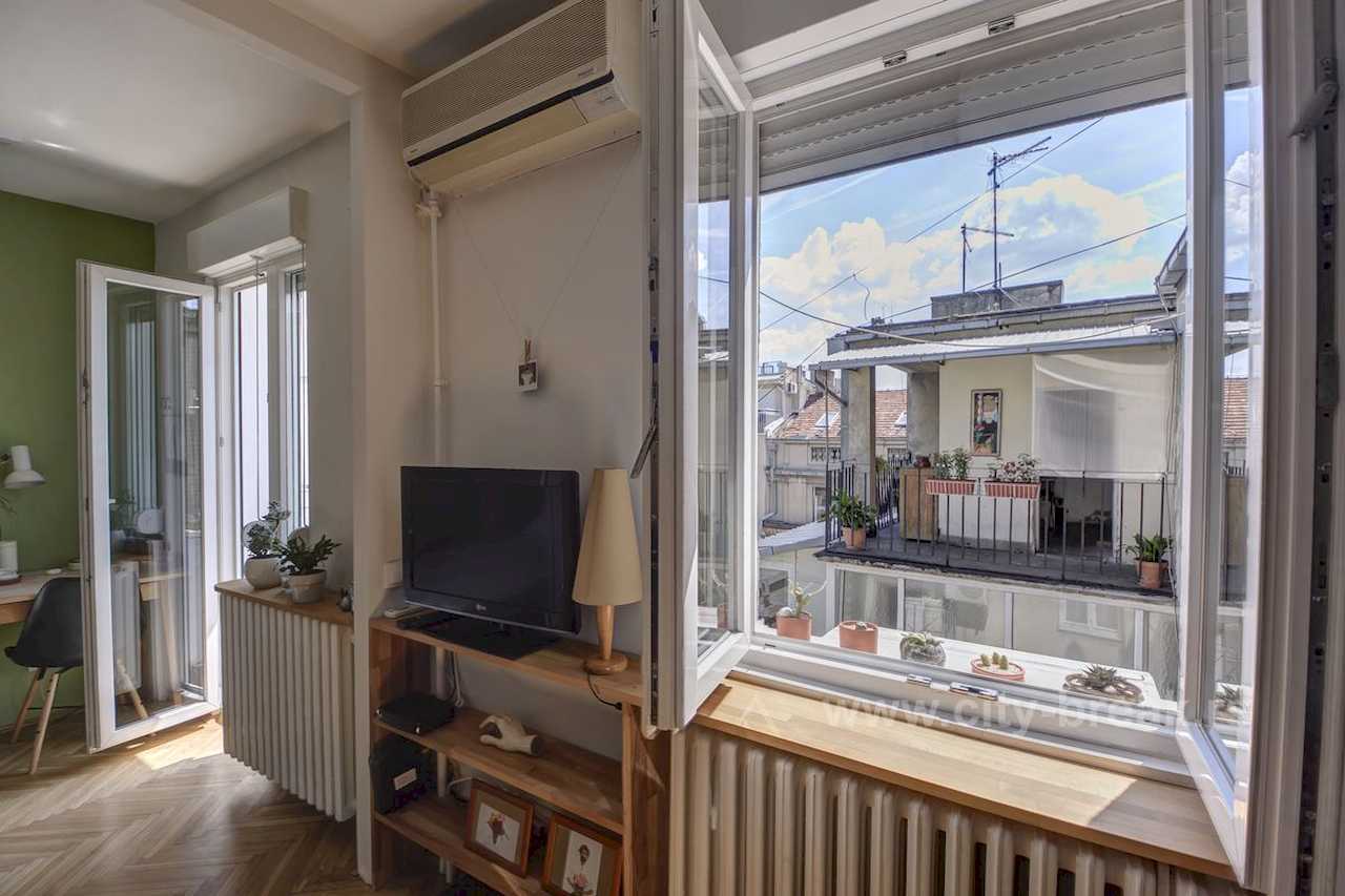 Apartman NINA (Vračar, Beograd) – otvoren prozor sa pogledom na grad, TV na drvenoj polici i biljke na klupi