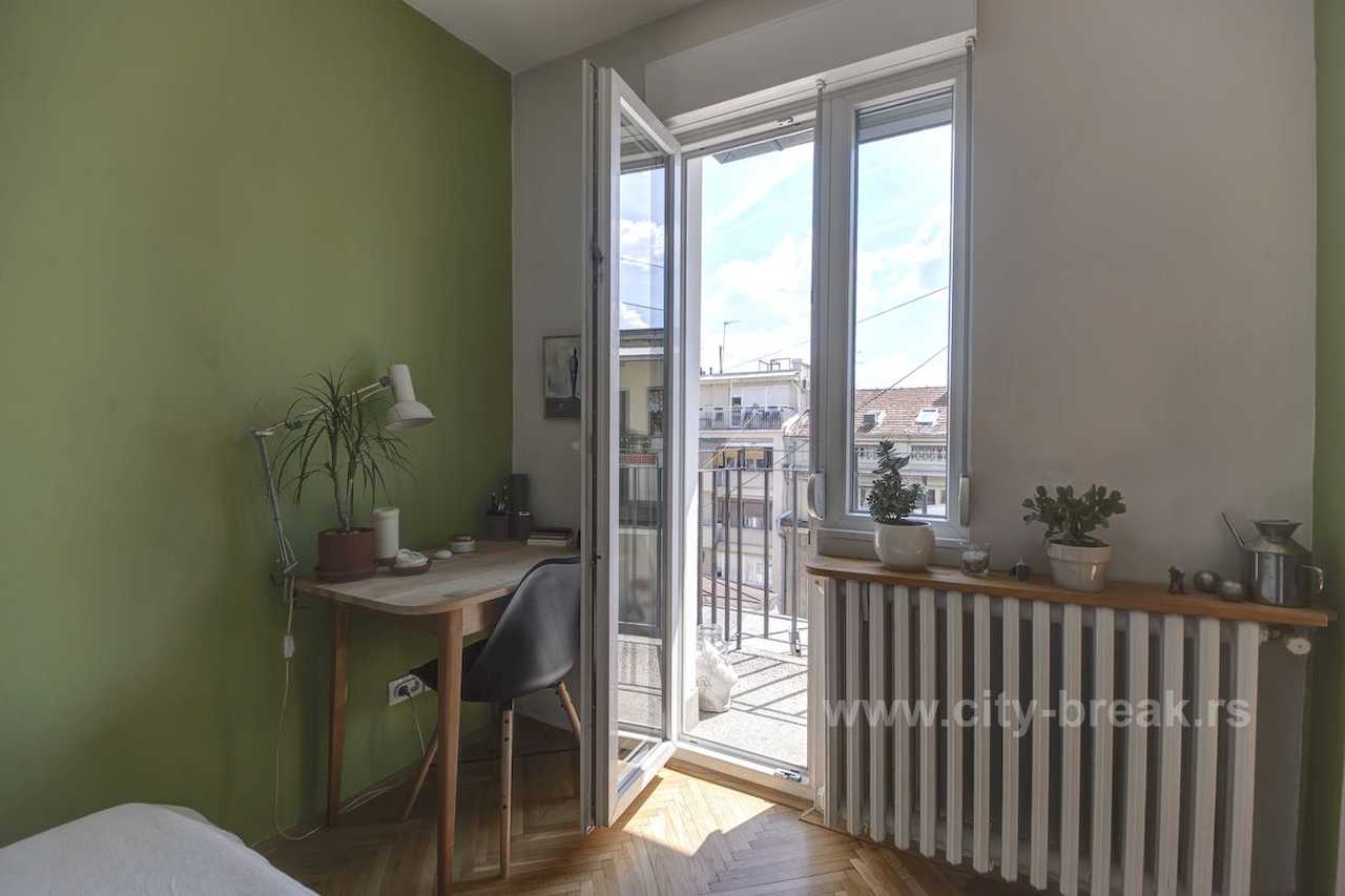 Apartman NINA (Vračar, Beograd) – radni kutak sa drvenim stolom pored otvorenih balkonskih vrata i zelenim zidom