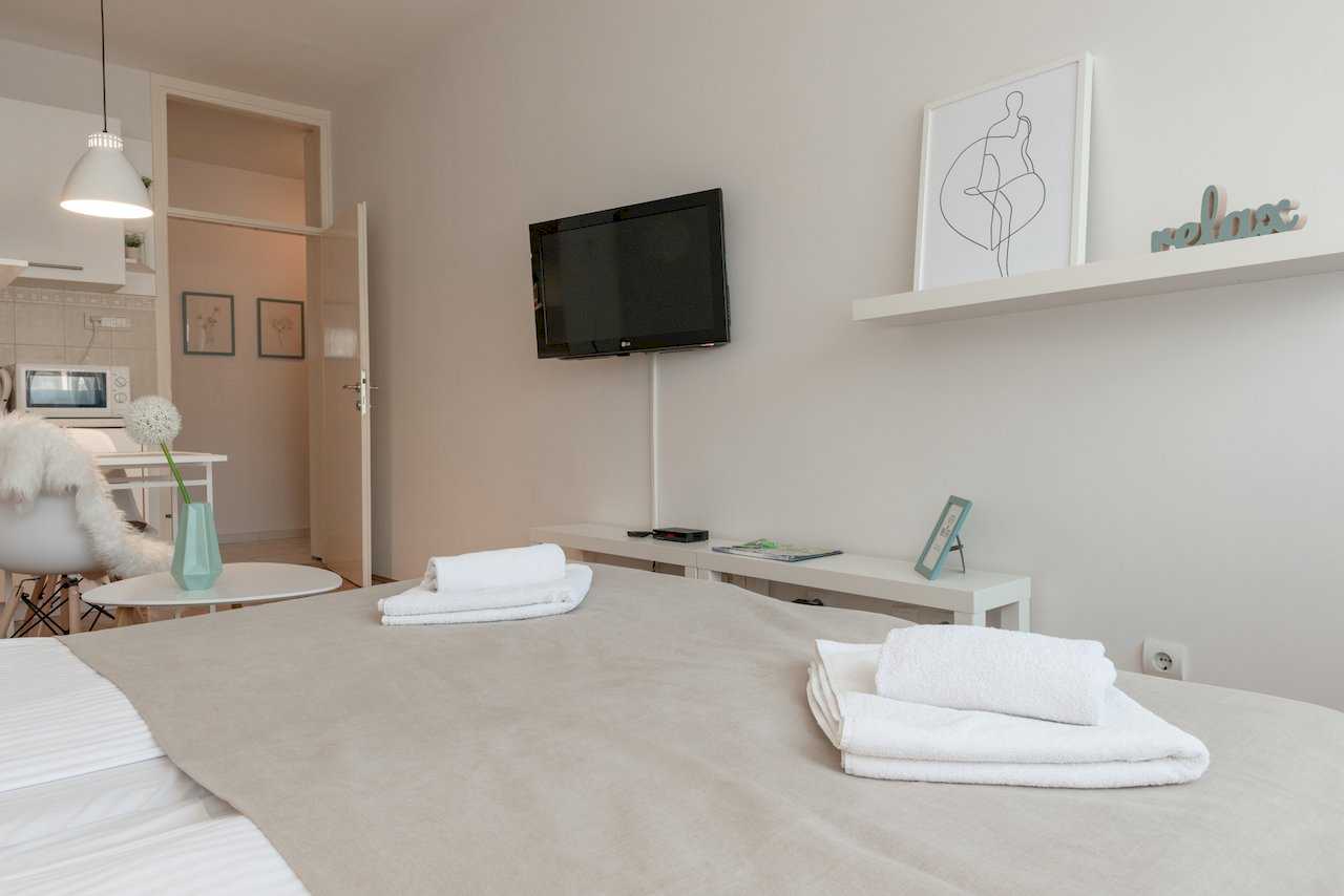 Sleeping area with bed, wall-mounted TV, and doorway toward the kitchen – Apartment Oaza – City Break Apartments
