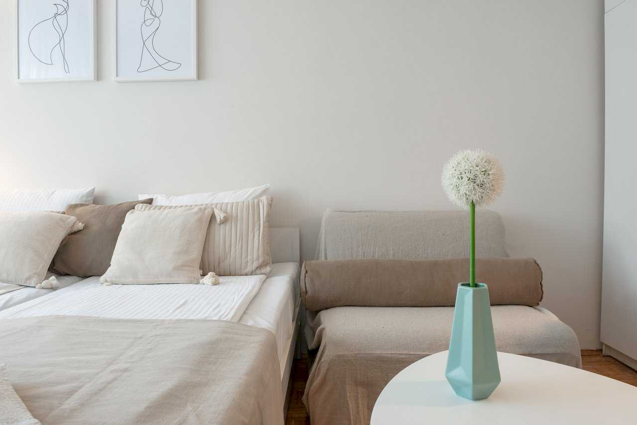 Bed with armchair, minimalist wall art, and turquoise vase on a side table – Apartment Oaza – City Break Apartments