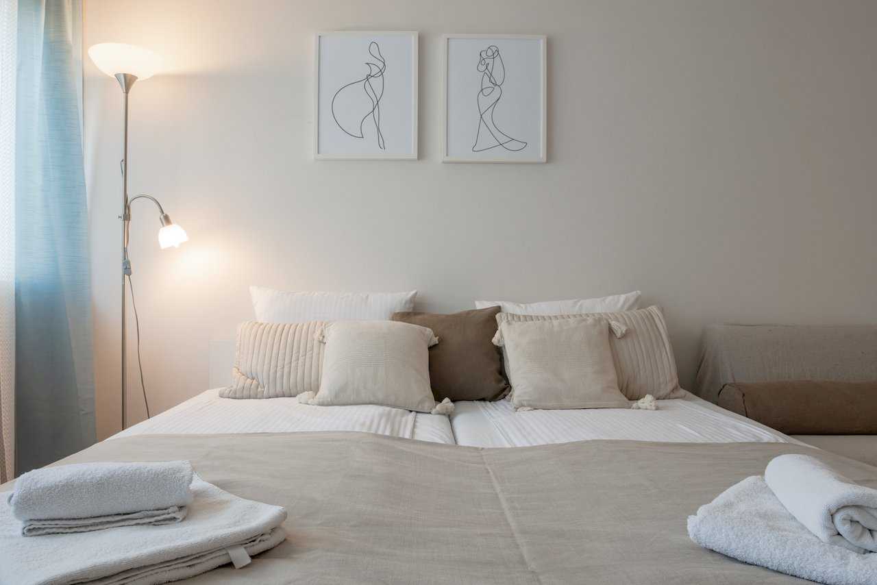 Double bed with decorative pillows, framed line art, and floor lamp – Apartment Oaza – City Break Apartments