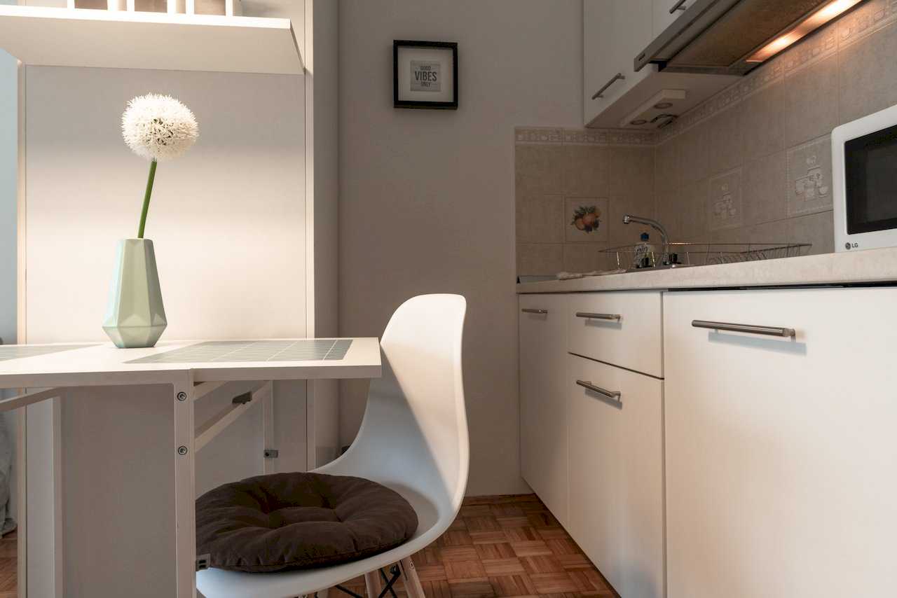 Kitchen corner with white cabinets, dining table, and framed wall sign – Apartment Oaza – City Break Apartments