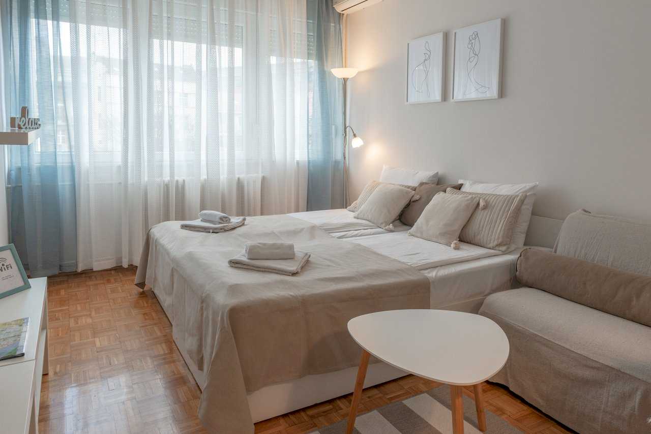 Bedroom with double bed, triangular white side table, and large window – Apartment Oaza – City Break Apartments