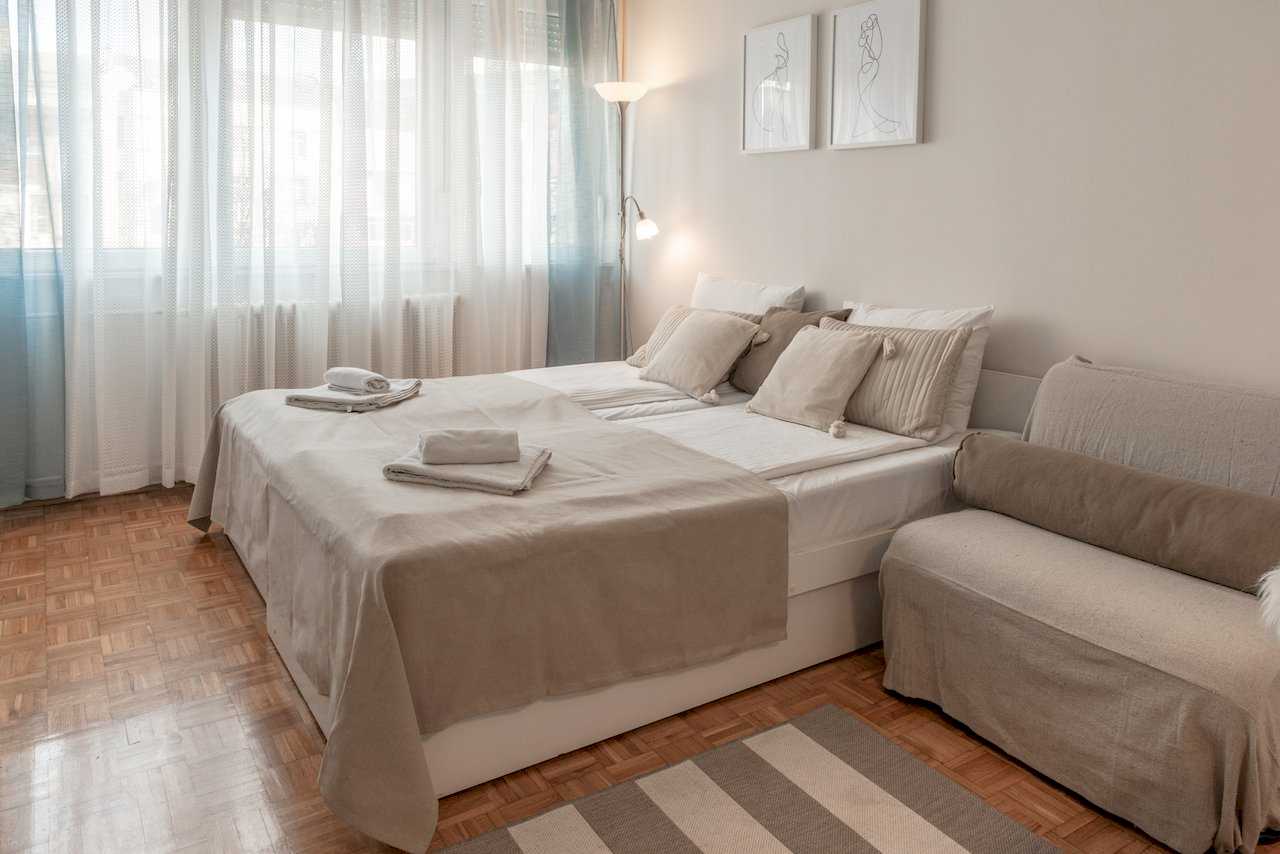 Bedroom with double bed, striped rug on parquet, and curtained window – Apartment Oaza – City Break Apartments