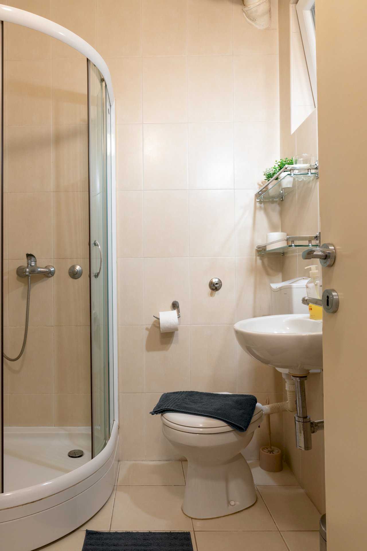 Compact bathroom with shower, toilet, wall sink, and glass shelves – Apartment Oaza – City Break Apartments