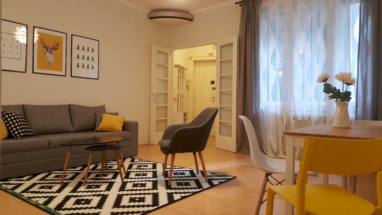 Living area with coffee table, sofa, black-and-white rug, and dining corner; window with curtains and double doors to hallway – Apartment Opera – City Break Apartments