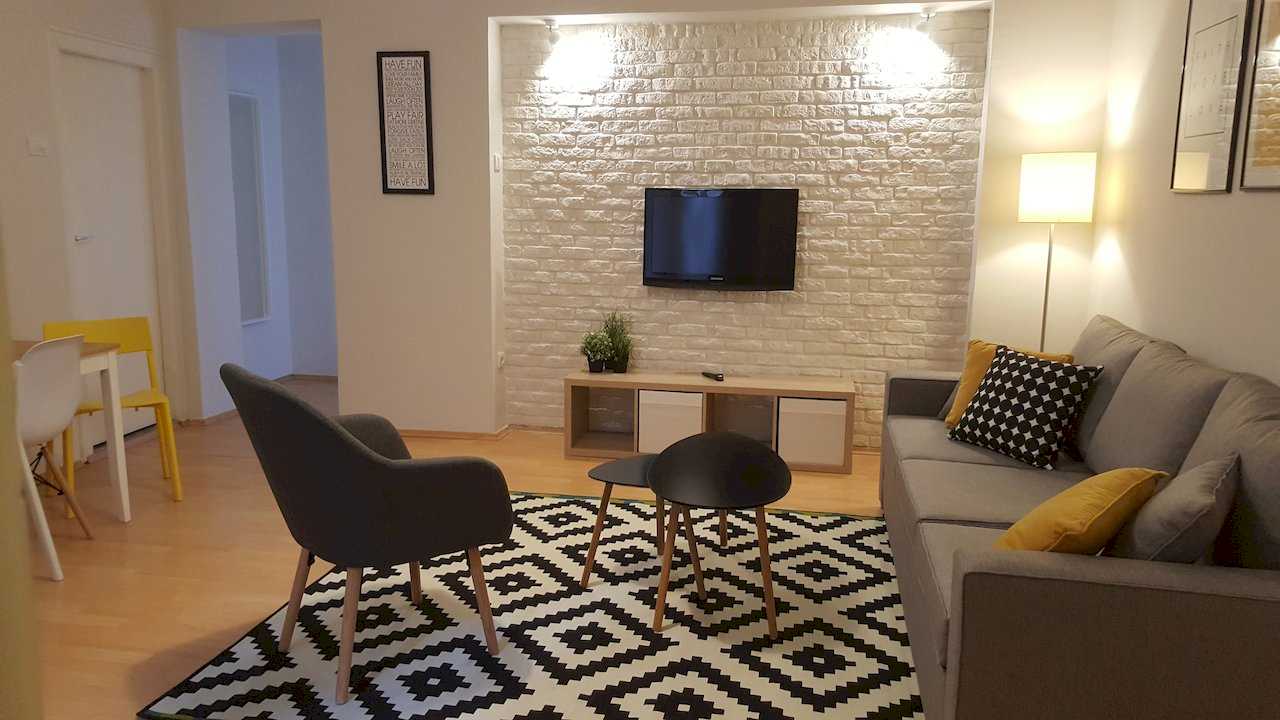 Living room with two round nesting coffee tables, armchair, geometric rug, TV on white brick wall, and floor lamp – Apartment Opera – City Break Apartments