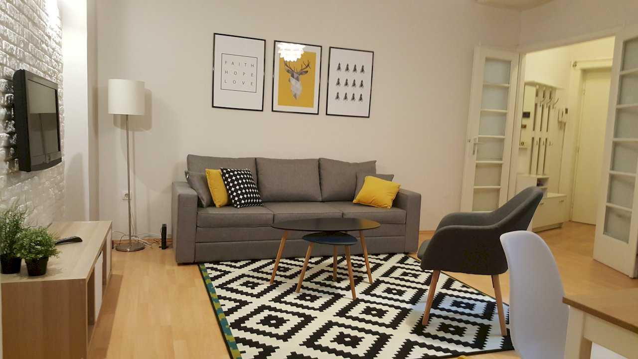 Living room with sofa, coffee table on rug, three framed prints above the sofa, and view toward the hallway – Apartment Opera – City Break Apartments