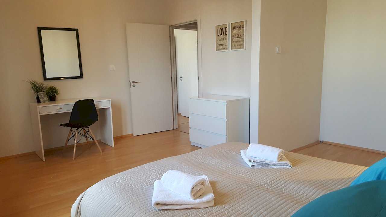 Bedroom with towels on the bed in foreground, desk with mirror, white dresser, and LOVE and HAPPINESS wall art – Apartment Opera – City Break Apartments