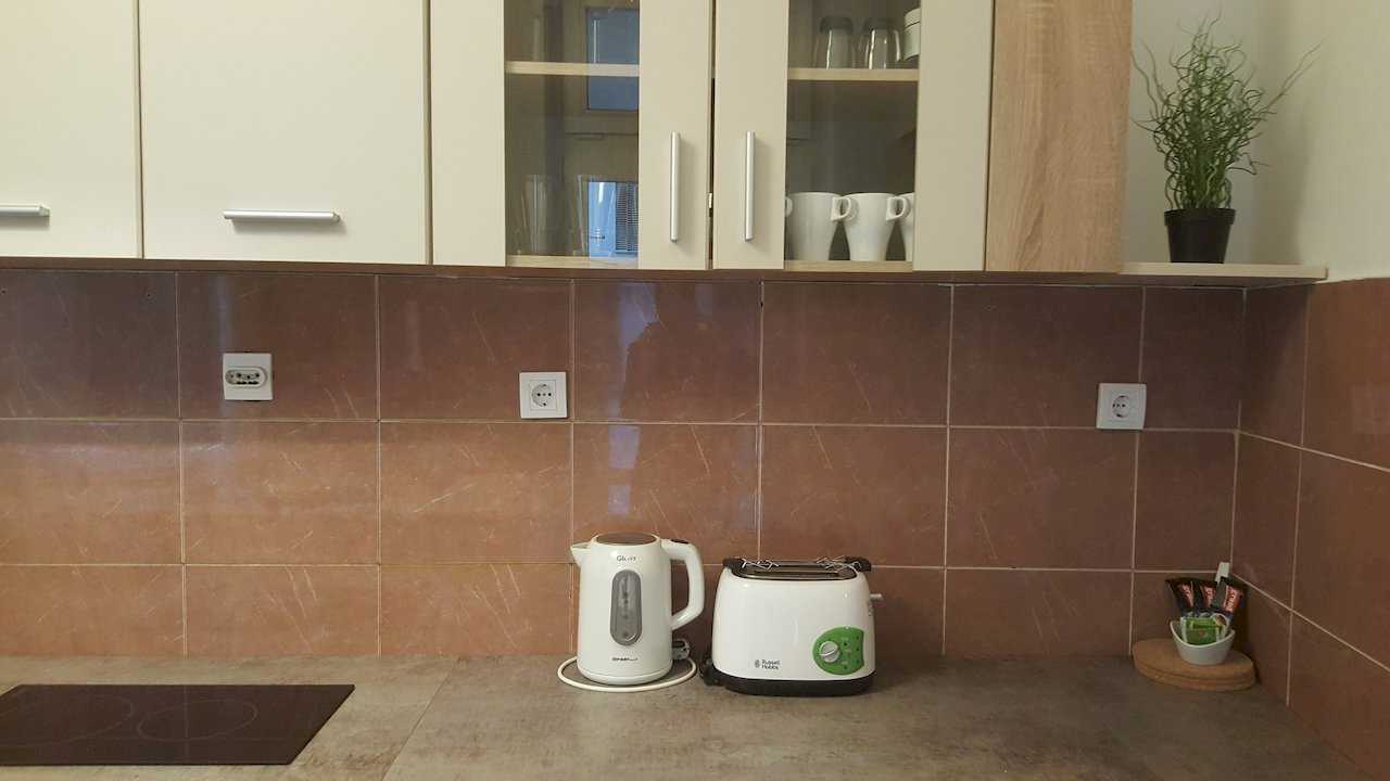 Kitchen counter with kettle, toaster, tea and coffee setup, glass-front upper cabinets, and terracotta tile backsplash – Apartment Opera – City Break Apartments