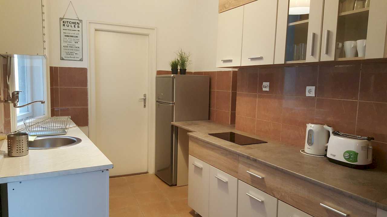 Kitchen with sink, fridge, glass-ceramic cooktop, white cabinets, terracotta backsplash, and framed Kitchen Rules sign – Apartment Opera – City Break Apartments
