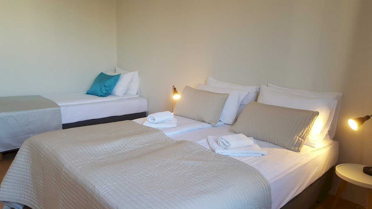 Room with double bed in front and single bed against far wall with a turquoise accent pillow – Apartment Opera – City Break Apartments