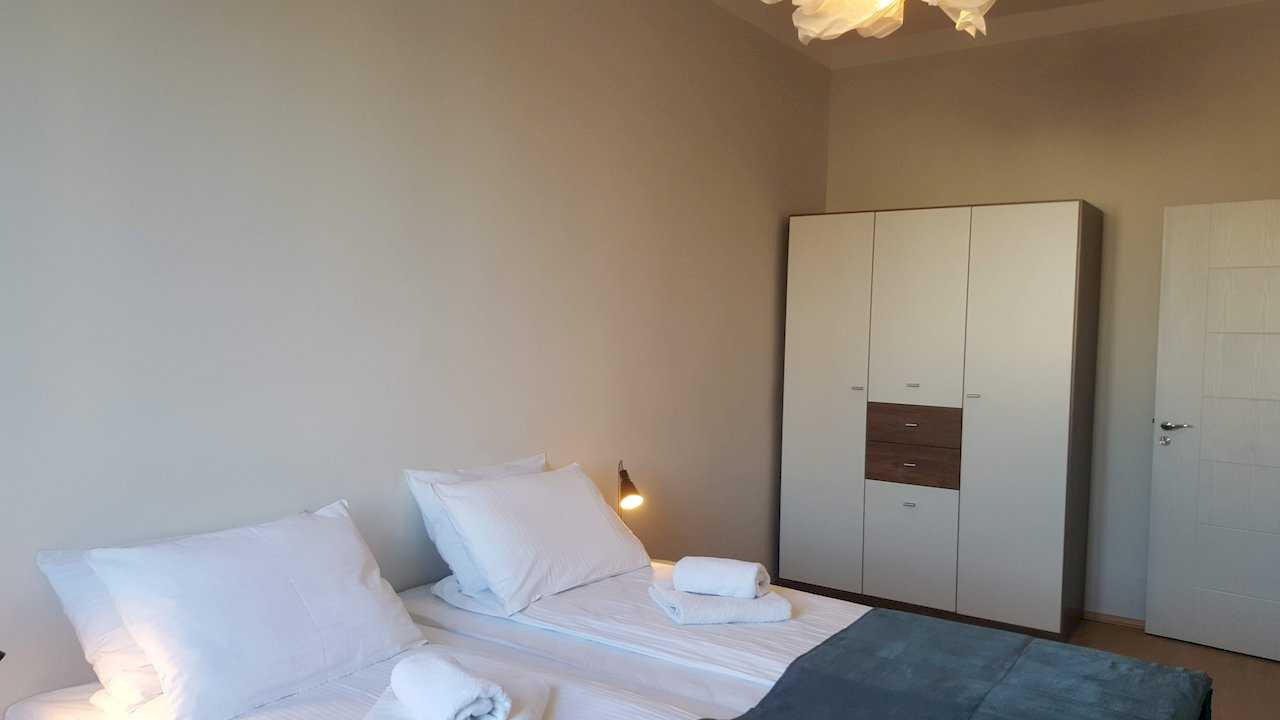 Bedroom with two joined singles, large three-door wardrobe, dark throw blanket, and wall-mounted reading lamps – Apartment Opera – City Break Apartments