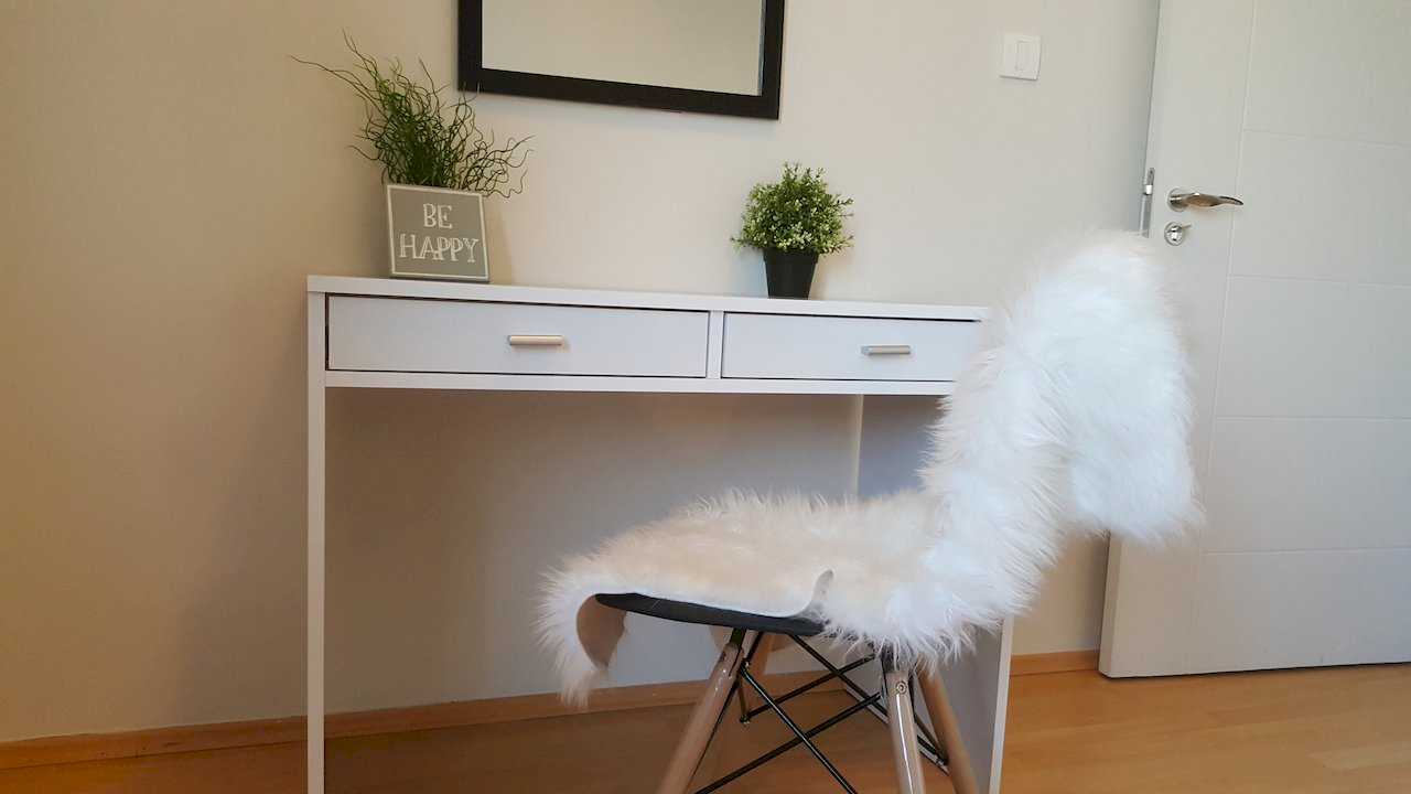White desk with drawers, chair with white faux fur, BE HAPPY plant block, small plant, and black-framed mirror – Apartment Opera – City Break Apartments