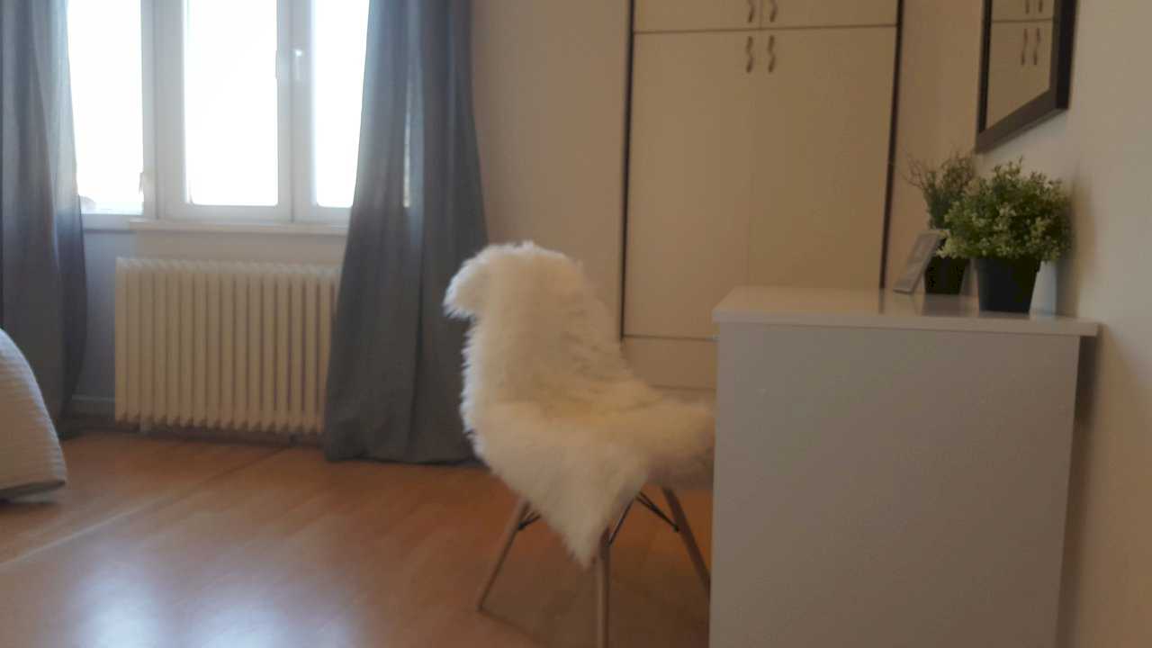 Window with grey curtains, white built-in wardrobe, desk with faux-fur-covered chair – Apartment Opera – City Break Apartments