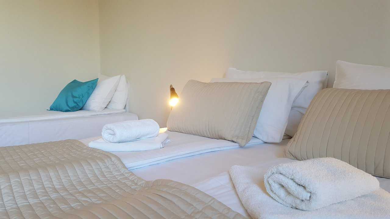 Sleeping arrangement with joined singles in foreground and extra single bed in background with turquoise pillow – Apartment Opera – City Break Apartments