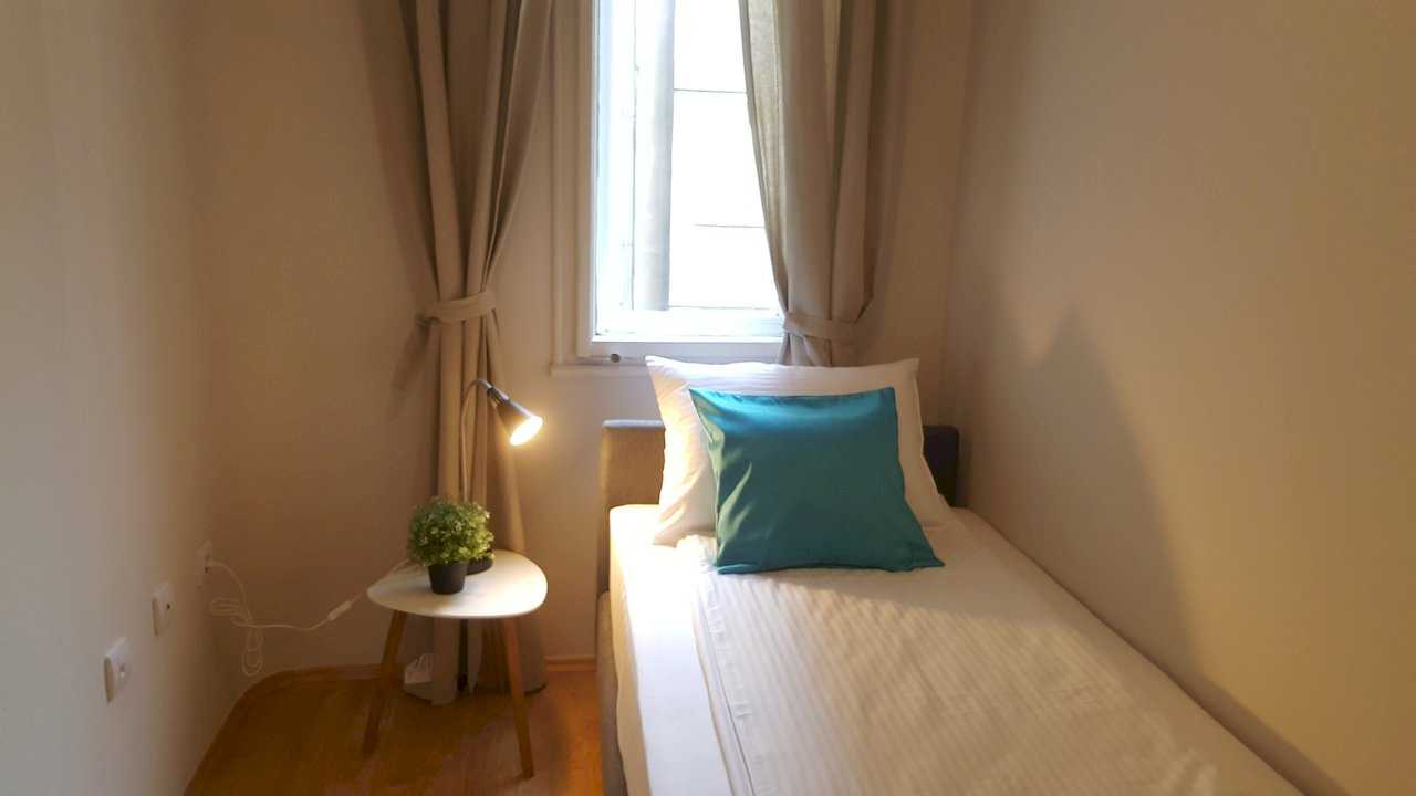Single bed with striped white bedding, turquoise pillow, and nightstand with lamp and plant – Apartment Opera – City Break Apartments
