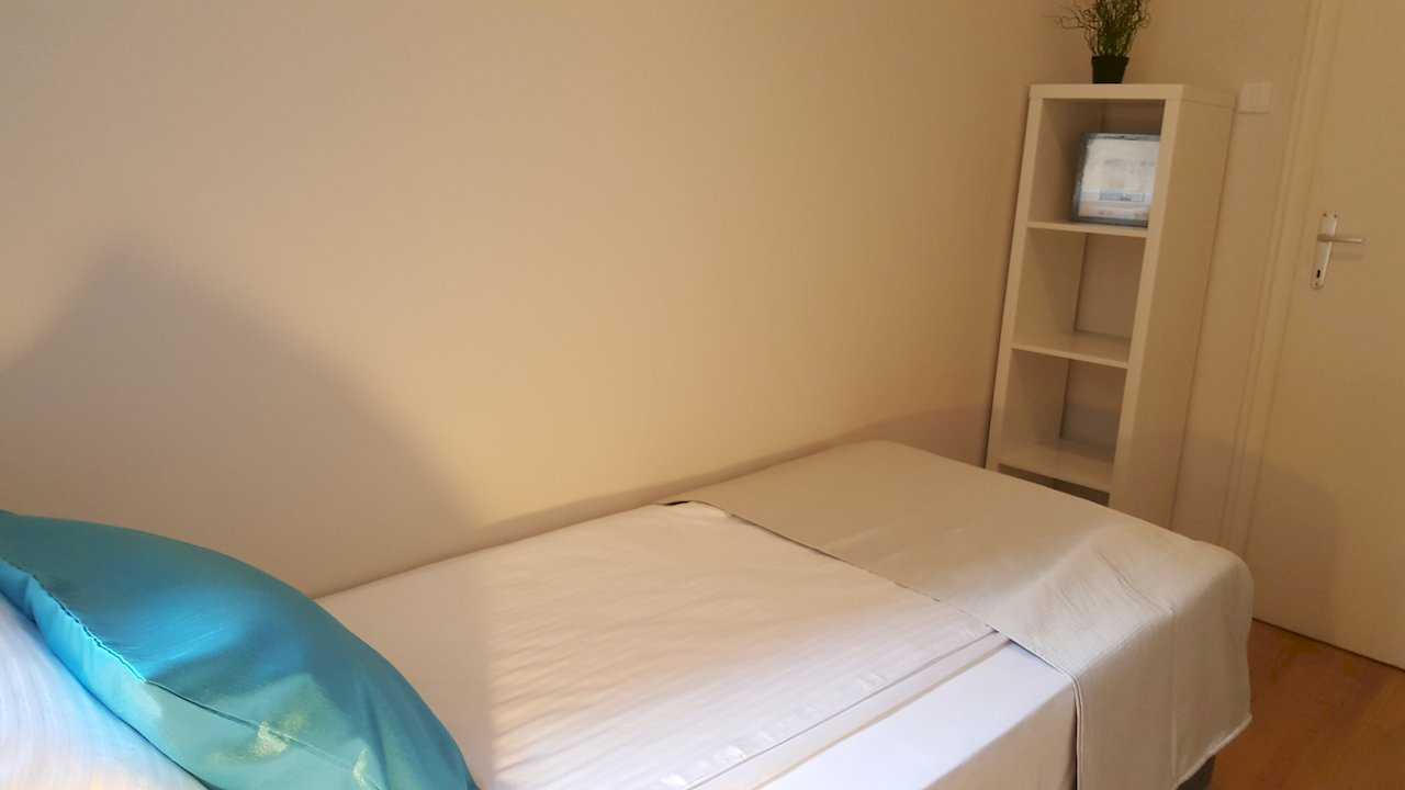 Single bed with turquoise pillow, beige runner, and white cube shelving unit in the corner – Apartment Opera – City Break Apartments