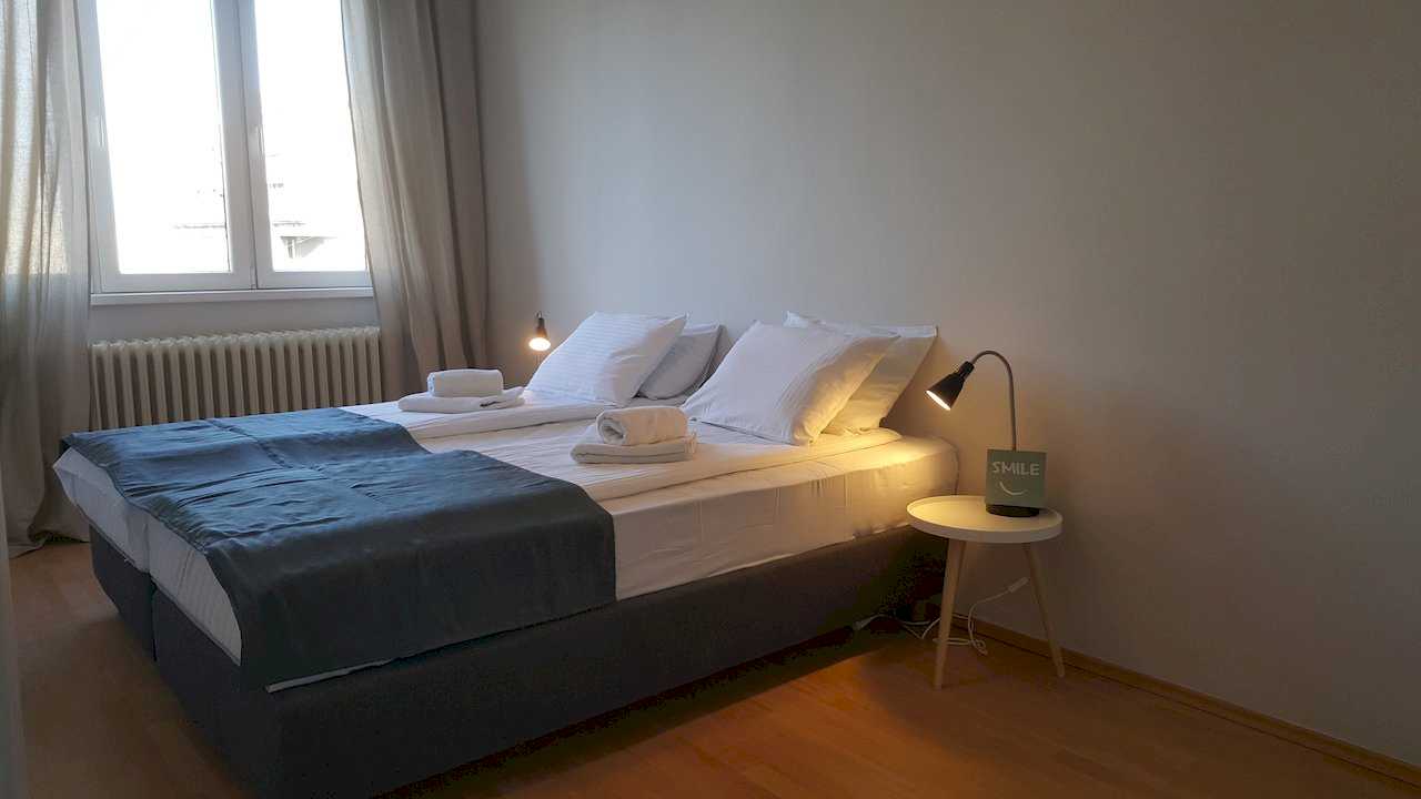 Bedroom with double bed, white linens, dark throw, rolled towels, bedside lamps, and SMILE desk sign – Apartment Opera – City Break Apartments