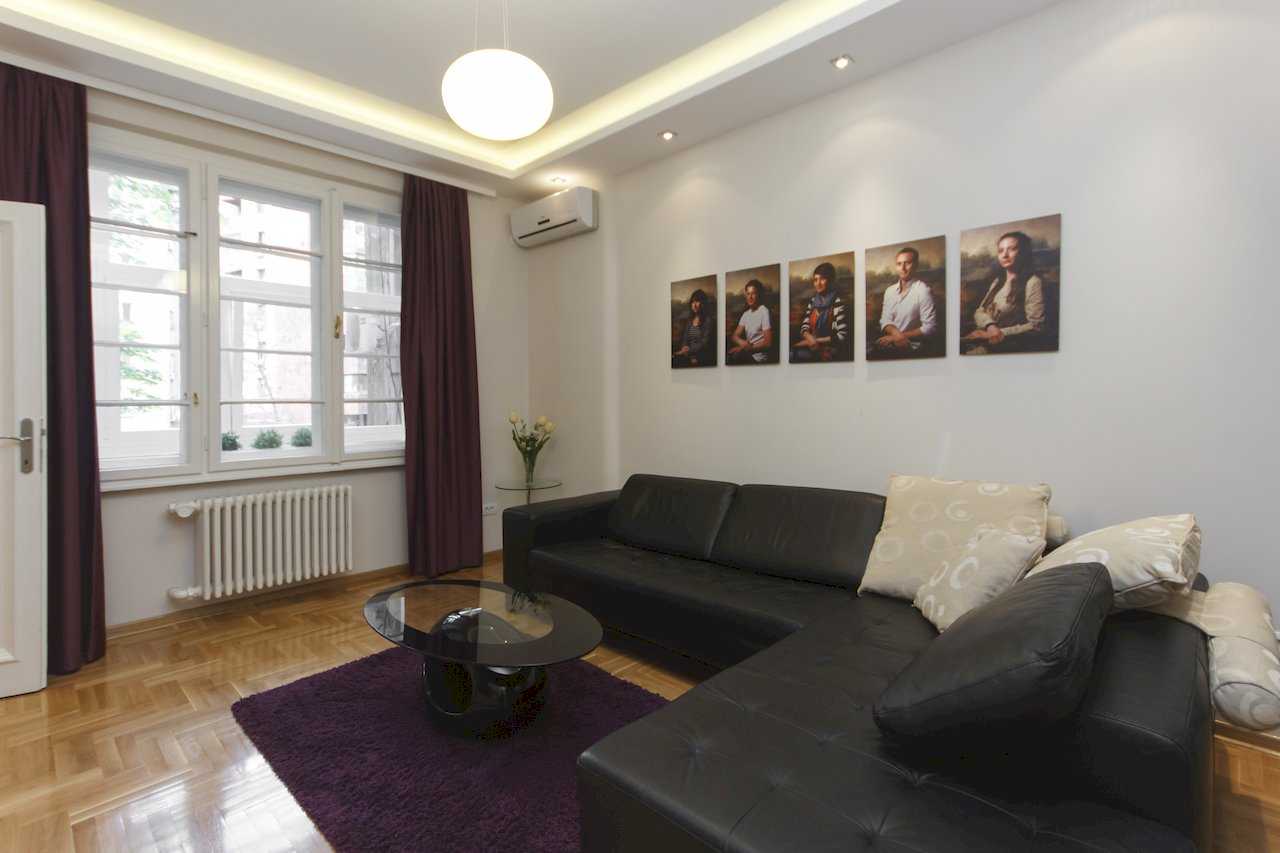 Apartment Parlament 2 (Vlajkovićeva Street, Belgrade) – living room with corner sofa, portrait gallery wall and large window
