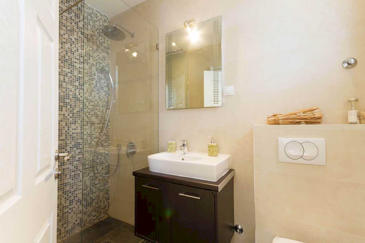 Bathroom with glass shower enclosure, mosaic shower wall, white vessel sink on dark vanity and mirror – Apartment Trg 1 – City Break Apartments