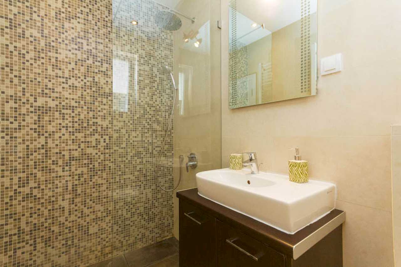 Bathroom detail: shower with mosaic wall, white vessel sink on dark cabinet and large mirror – Apartment Trg 1 – City Break Apartments