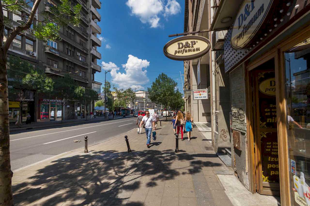 Pedestrian zone along the street: perfumery shopfront, wide pavement, pedestrians and mid-rise buildings – Apartment Trg 1 – City Break Apartments