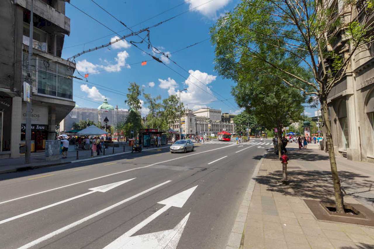 View toward Republic Square: National Museum with green dome, National Theatre, buses and trolleybus wires overhead – Apartment Trg 1 – City Break Apartments