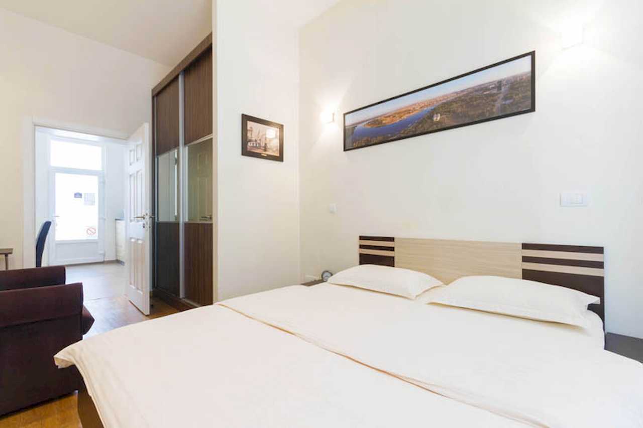 Bedroom with double bed, panoramic print above the bed, built-in mirrored wardrobe and open door toward the entrance – Apartment Trg 1 – City Break Apartments