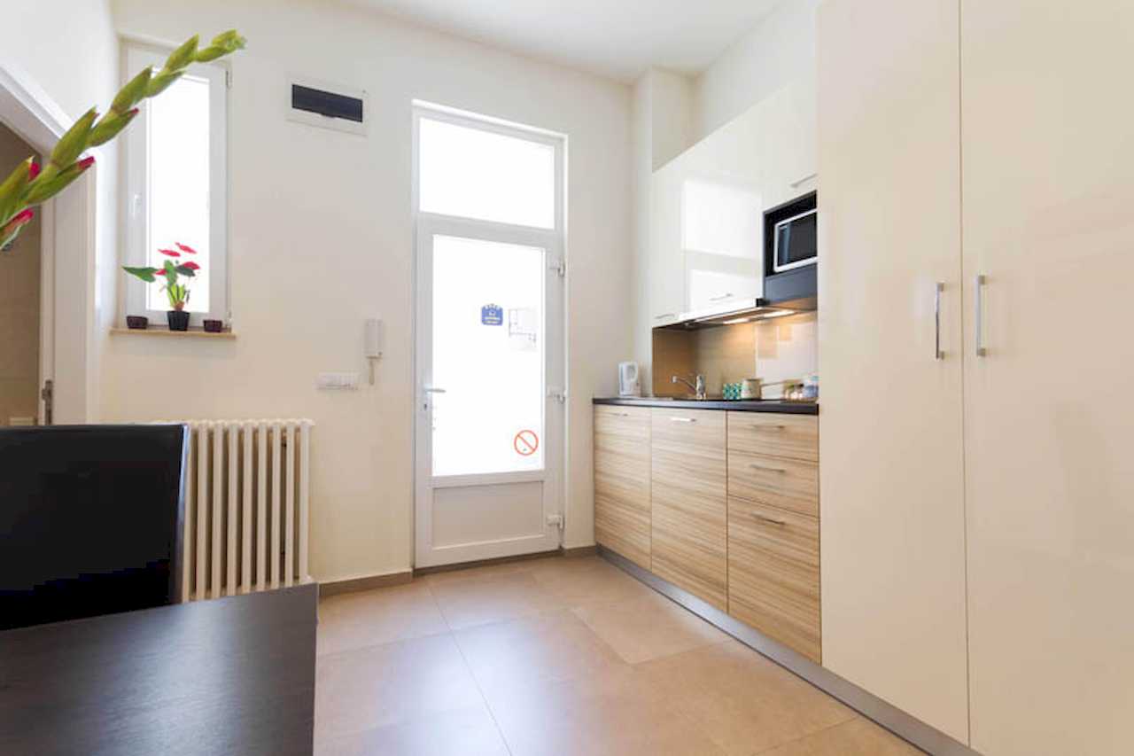 Kitchenette with white and wood cabinets, full-height white wardrobe, glass doors to the balcony and part of the dining table – Apartment Trg 1 – City Break Apartments