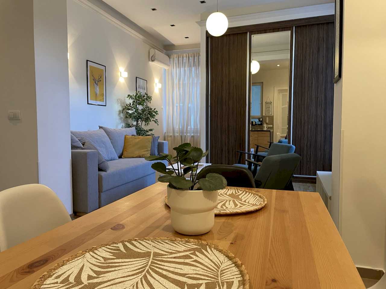 Pogled sa trpezarijskog stola na dnevnu sobu sa sofom i plakarom – Apartman Trg 2 – City Break Apartments