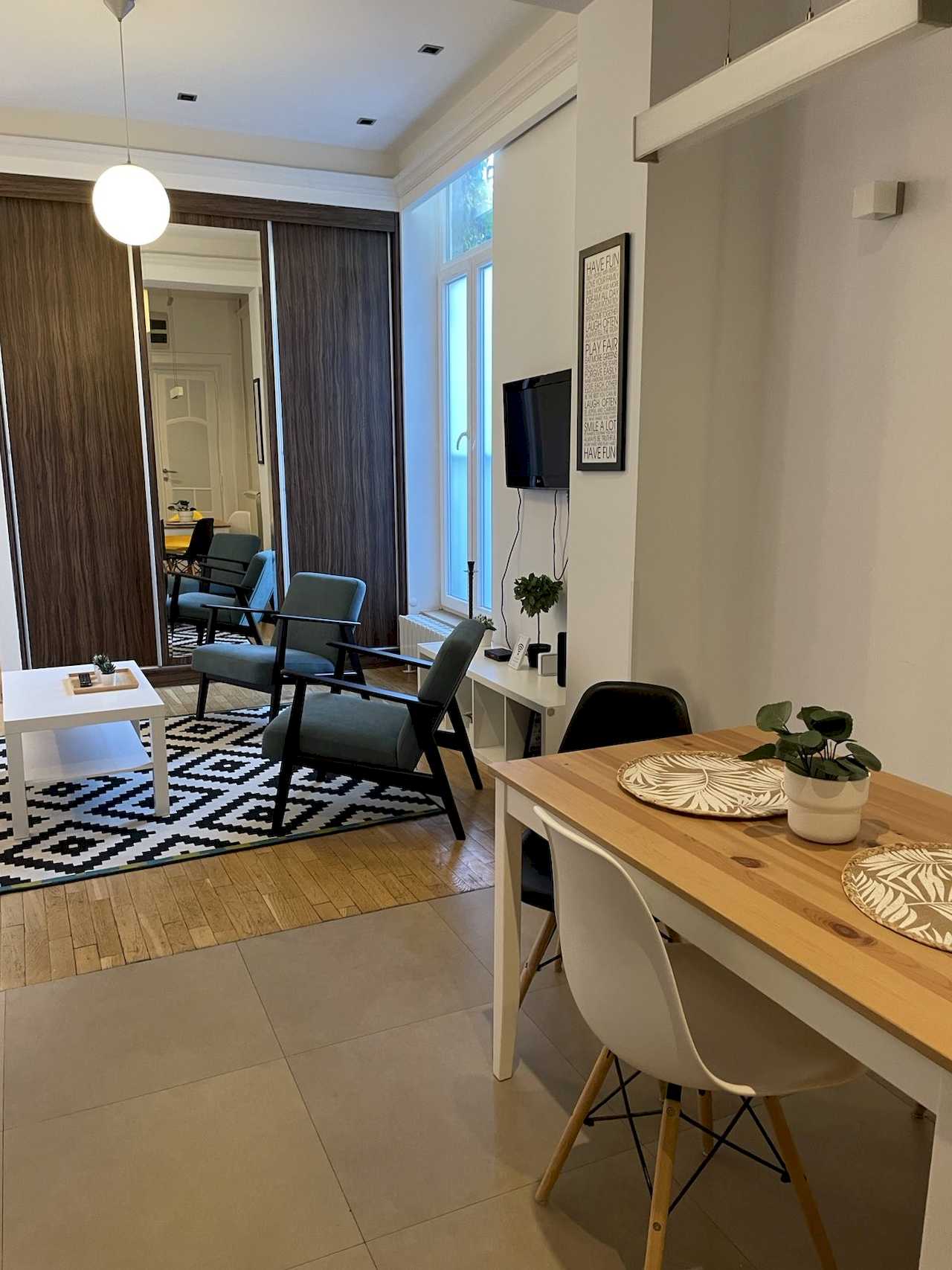 Open space sa trpezarijom, tirkiznim foteljama, TV-om i plakarom sa ogledalom – Apartman Trg 2 – City Break Apartments