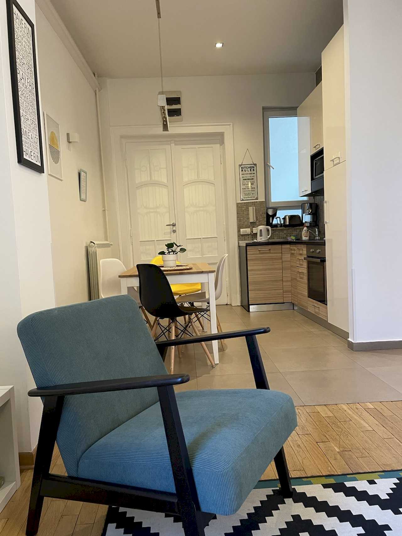 Dnevni boravak sa foteljom, trpezarijom i kuhinjom u pozadini – Apartman Trg 2 – City Break Apartments