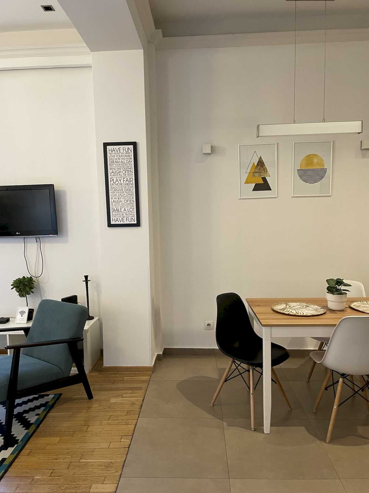 Trpezarija sa umetničkim slikama i pogled na TV zonu sa plavom foteljom – Apartman Trg 2 – City Break Apartments
