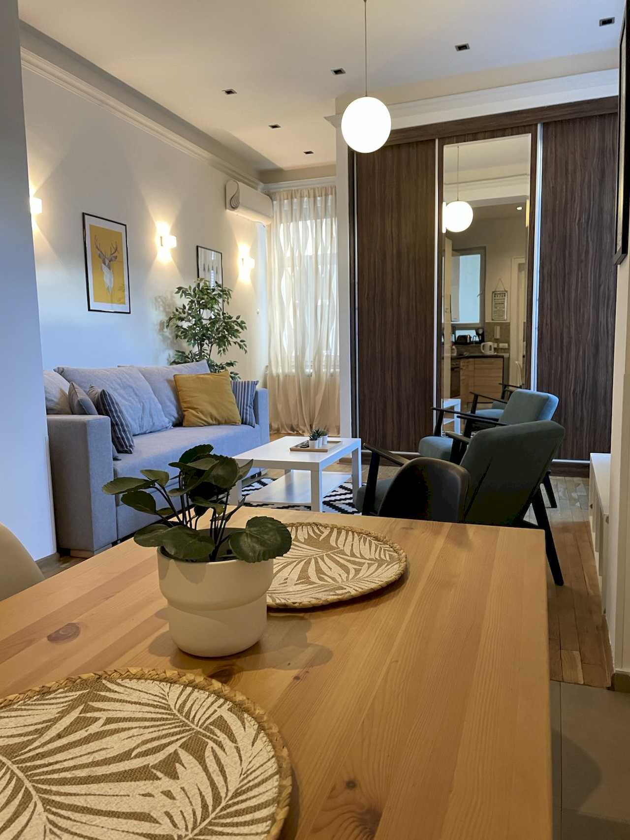 Dnevna soba sa trpezarijskim stolom, svetlom sofom, foteljama i plakarom sa ogledalom – Apartman Trg 2 – City Break Apartments