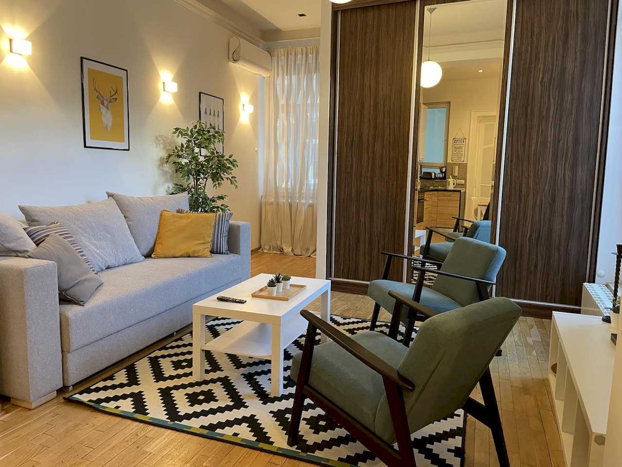 Dnevna soba sa sivom sofom, tirkiznim foteljama i ogledalom na plakaru – Apartman Trg 2 – City Break Apartments